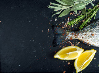 Fototapeta na wymiar Tail of fresh raw Dorado or sea bream fish on black slate stone board with spices, herbs, lemon and salt