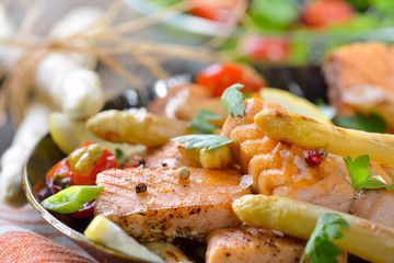 Gebratener bayerischer Spargel mit Lachsstreifen in der Eisenpfanne mit Rucola-Beilagensalat serviert - Roasted  white asparagus with fried salmon served in an iron frying pan with a rocket side salad