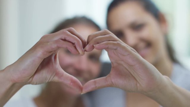  Portrait of young gay couple at home making a heart shape with their hands.
