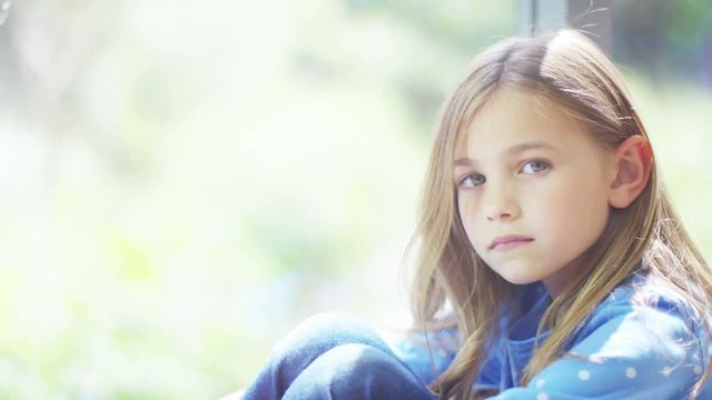  Portrait of unhappy little girl sitting alone by a window.