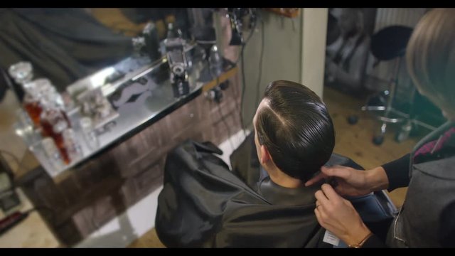  Female stylist preparing to cut a customer's hair in traditional retro barber shop. 