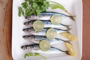 sardines with lemon wedges and parsley on plate with wooden background colored