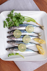 sardines with lemon wedges and parsley on plate with wooden background colored