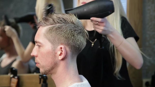 Woman barber drying man's head, finishing the haircut, styling the hairdo