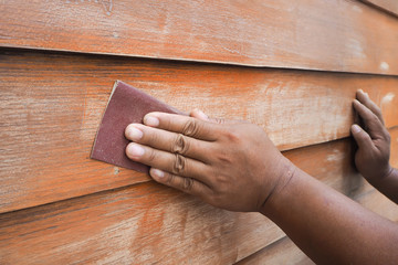 Human hands scrubbing wood wall by sandpaper.