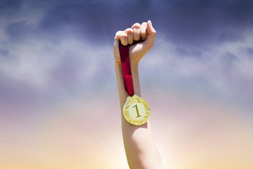 Composite image of hand holding a gold medal on white background