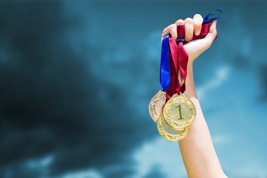 Composite image of hand holding three medals on white background