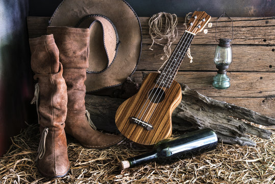 Still life photography with ukulele on american west rodeo brown felt  cowboy hat and traditional leather boots in vintage ranch barn background  Stock Photo | Adobe Stock