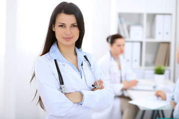 Brunette female doctor on the background of colleagues talking to each other in hospital