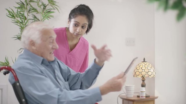  Caring home support nurse helping elderly man to use a computer