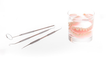 dentures in glass of water and tools on white background
