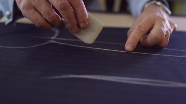  Close up on hands of a tailor working in his shop, drawing template on a piece of fabric. Shot on RED Epic.
