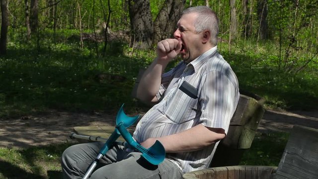 Tired disabled man with crutches on bench in the park