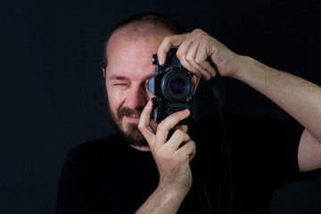     Man on black background in low key, holding analog camera and taking photos 