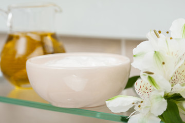 Natural oil, nourishing mask and flowers on a bathroom shelf