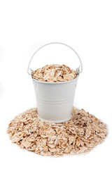 White bucket full of oat flakes, stands on a heap oat flakes