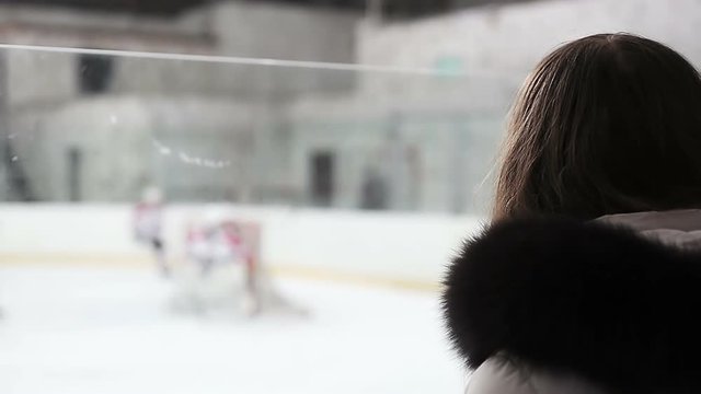 Young woman watching hockey match, worried about score and players on ice rink