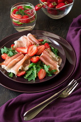 Fresh salad with strawberry, arugula and prosciutto on purple plate. Low key