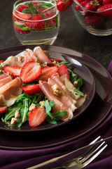 Fresh salad with strawberry, arugula and prosciutto on purple plate. Low key