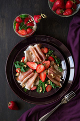 Fresh salad with strawberry, arugula and prosciutto on purple plate. Low key