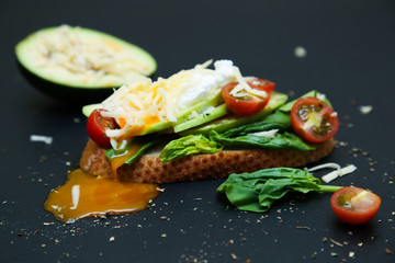 Healthy toast with avocado, tomatoes, spinach and poached egg.
