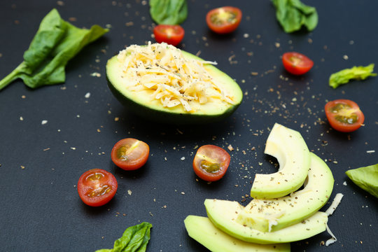 Sliced avocado and tomatoes, spinach leaves on black background.