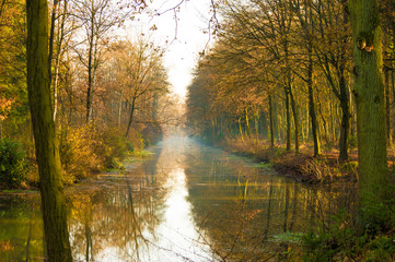 Canal in a autumn colored forest with trees reflecting on the water