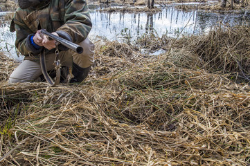 The hunter sits on the swamp in the forest and holding an old hunting rifle