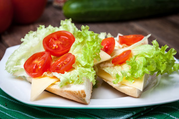 Delicious sandwich with tomatoes, cheese and lettuce on wooden table.