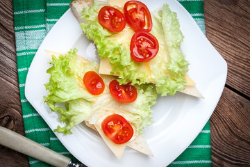 Delicious sandwich with tomatoes, cheese and lettuce on wooden table.