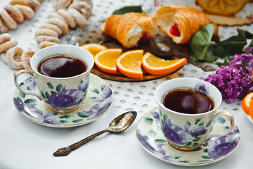 Beautiful and healthy Breakfast: croissants and coffee on the table with oranges and lilac flowers
