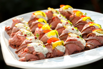 Plate of sliced, rolled and garnished roast beef canapes. On bla