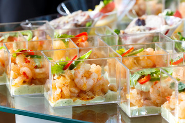 Buffet table detail of prawn canapes in plastic dishes.