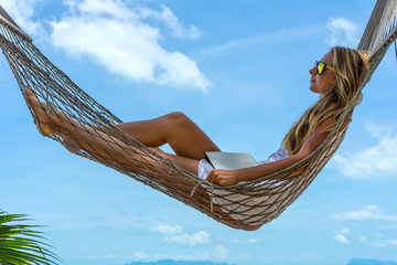 Young woman resting in hammock with laptop on a tropical beach