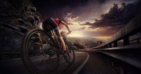 Fototapeta na wymiar Cyclist riding a bike on an open road to the sunset