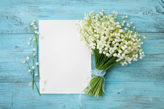 Fototapeta Bouquet of flowers lily of the valley and empty paper sheet on turquoise rustic table from above, beautiful vintage card, top view, copy space for text, flat lay