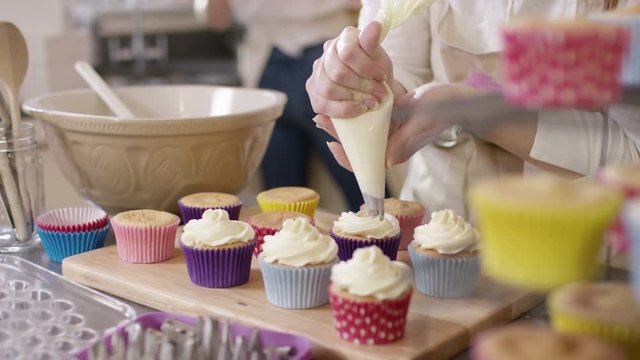  Woman with home bakery business piping cream onto cupcakes