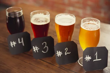Gordijnen Glasses with different sorts of craft beer and numbering on wooden table. Retro stylization © Africa Studio