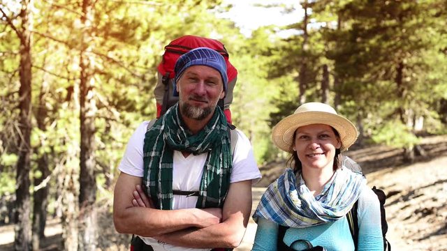 Couple during travel, hiking, standing on trail in forest, looking at camera and at each other, smiling and laughing. Sunny day in Cyprus.