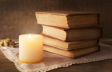 Books, flowers and candle on napkin on wooden table on wooden wall background