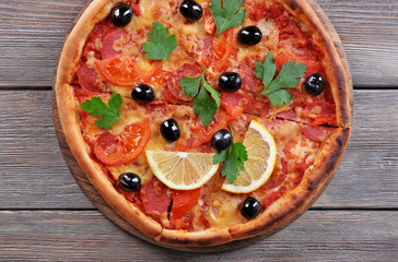 Delicious Italian pizza with black olives and slices of lemon on wooden table background