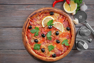 Tasty pizza with spices and round knife on board and wooden table background