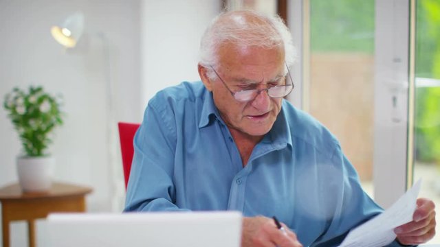  Frustrated senior man working on a laptop computer & looking at paperwork. Shot on RED Epic.