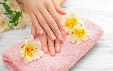 Obraz na płótnie Canvas Spa concept. Woman hands with beautiful manicure and flowers on towel, close up