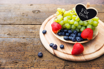 Fresh mix of seasonal fruits in a bowl on wooden table, heart wi