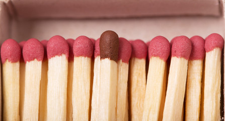 Macro. Single brown matchstick among red, concept crowd