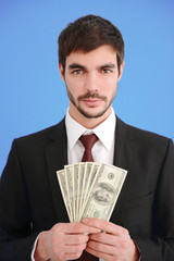 Attractive man in a suit holding fan of dollar banknotes on blue background