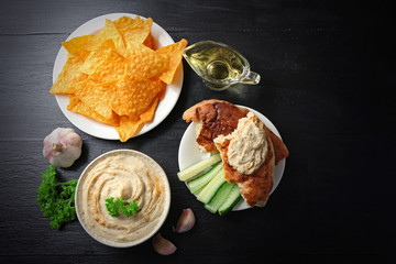 Ceramic bowl of tasty hummus with chips and parsley on table