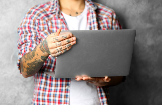 Young man with tattoo holding laptop on grey background
