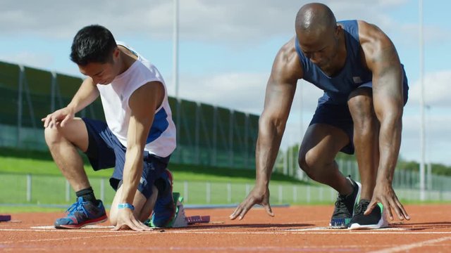  2 athletes get into position at running track starting line before a race